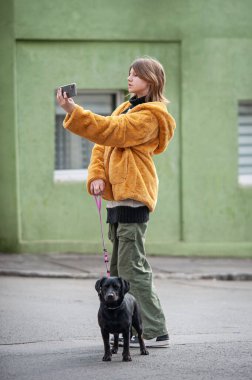 Sarı kürklü, sosyal medya etkileyicisi, siyah köpeğiyle şehirde gezen, akıllı telefon kullanan genç ve güzel bir kadın..