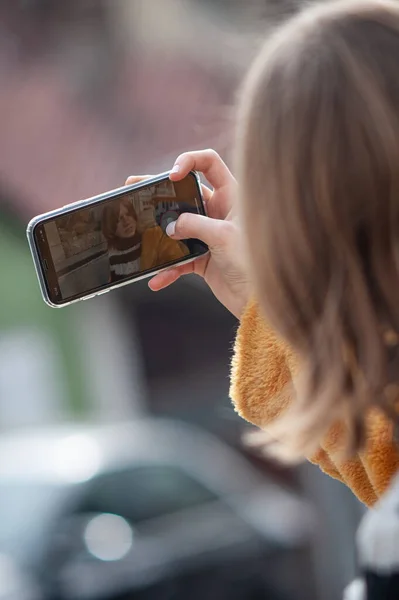 身穿黄色毛皮外套的年轻漂亮女人是社交媒体的影响者 她用智能手机 带着她的黑狗在城市的街道上行走 — 图库照片