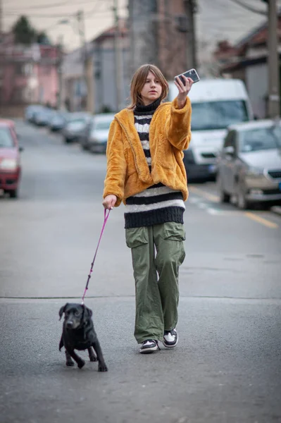 Sarı kürklü, sosyal medya etkileyicisi, siyah köpeğiyle şehirde gezen, akıllı telefon kullanan genç ve güzel bir kadın..