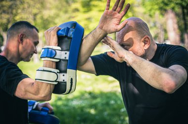 Muay Thai antrenörü odaklanma eldiveni tutuyor. Dirsek tekmesi tekniği eğitimi ve pedlerle gösteri. Dövüş sanatları pratiği