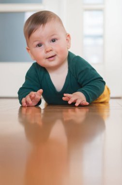 Sevimli, mutlu, gülümseyen bir erkek bebeğin portresi ev zemininde emekleyerek kameraya bakıyor. Neşe ve mutluluk kavramı. Ön manzara. Aşk ve aile duyguları