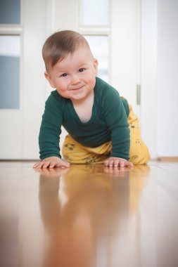Sevimli, mutlu, gülümseyen bir erkek bebeğin portresi ev zemininde emekleyerek kameraya bakıyor. Neşe ve mutluluk kavramı. Ön manzara. Aşk ve aile duyguları