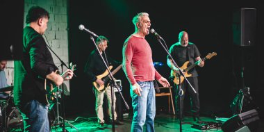 Punk rock müzik grubu sahnede canlı performans sergiliyor. Şarkıcı, bas gitarist, müzisyen ve davulcu.