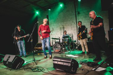 Punk rock müzik grubu sahnede canlı performans sergiliyor. Şarkıcı, bas gitarist, müzisyen ve davulcu.