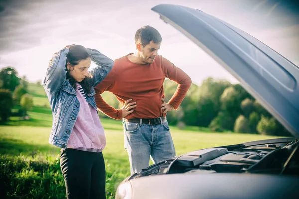 stock image A young couple had a car breakdown on the road. They stand very upset, open the hood and try to fix the broken engine