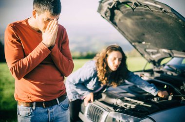 Genç bir çift yolda araba arızası yaşadı. Çok üzgün duruyorlar, kaputu açıp bozuk motoru tamir etmeye çalışıyorlar.