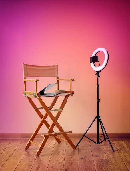 Director\'s chair, ring lights, digital camera with laptop and hats on colorful background with recording equipment