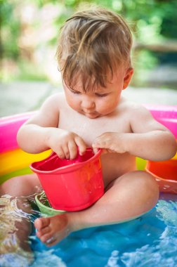 Küçük sevimli bir erkek bebek renkli bir havuzda banyo yaparken oyuncaklarla oynuyor. Yaz zamanı. Neşe ve mutluluk kavramı. Aşk ve aile duyguları