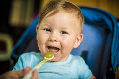 Beautiful baby boy eating porridge food, with a spoon. Hungry baby with open mouth enjoying food. Mother feeding her baby