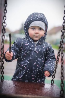 Sevimli erkek bebek parkta salıncağın yanında duruyor. Açık hava oyunları. Mutlu bir çocukluk. Çocuk eğlencesi