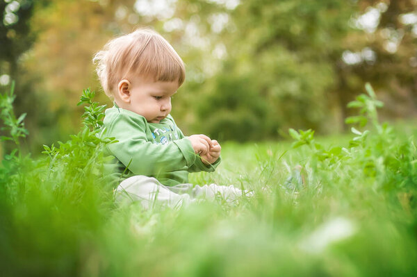 Cute baby having fun sitting on grass in sunshine day. Summer time, happy baby