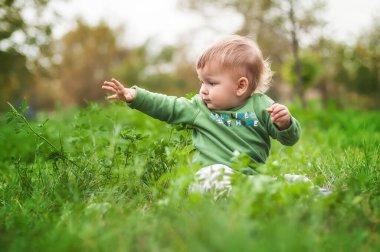 Güneşli bir günde çimenlerde oturarak eğlenen sevimli gülen bir bebek. Yaz zamanı, mutlu bebek