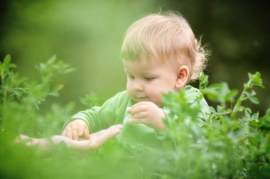 Güneşli bir günde çimenlerde oturarak eğlenen sevimli gülen bir bebek. Yaz zamanı, mutlu bebek