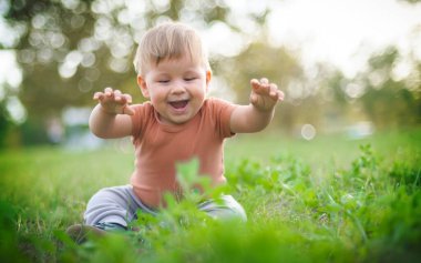 Güneşli bir günde çimenlerde oturarak eğlenen sevimli gülen bir bebek. Yaz zamanı, mutlu bebek