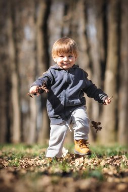 Bebekler sonbahar macerası. Meraklı çocuk yere düşen yaprakların arasına çömelmiş, doğanın mucizelerini keşfediyor. Çocuk dışarıda oynuyor.