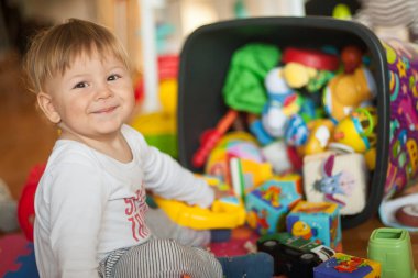Neşeli bir çocuk, canlı bir oyuncak çeşidinin ortasında oturur, oyunla uğraşırken mutlulukla ışıldar. Oda yaratıcılığa ilham veren renkli şeylerle dolu..