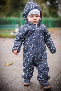 Rahat, desenli bir kar elbisesi içinde, bir erkek bebek yol boyunca geziniyor, taze havanın tadını çıkarırken sonbahar yapraklarının canlı renklerini alıyor..