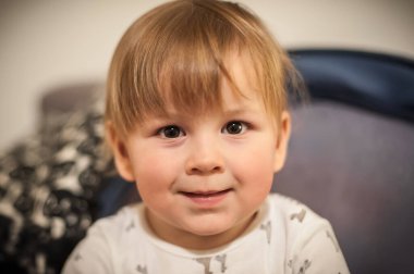 Açık kahverengi saçlı neşeli bir çocuk kameraya masumiyet ve neşe saçıyor. Sıcak atmosfer, bu keyifli anın neşeli ruhunu arttırır..