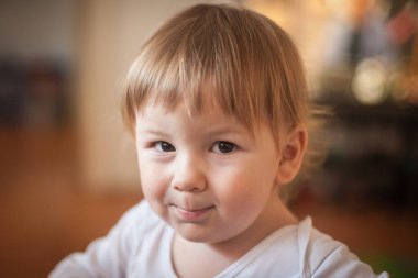 Sıcak, aydınlık bir odada, bir bebek oyuncaklarla dolu canlı çevrelerini keşfederken dudaklarında oynaşan utangaç bir gülümseme ve neşeli bir merakla bakıyor..
