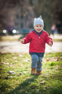 Canlı kırmızı ceketli ve gri şapkalı küçük bir çocuk yemyeşil bir parkta neşeyle yarışıyor. Kahkahaları kıtır sonbahar havasında yankılanıyor. Düşen yapraklarla çevrili..
