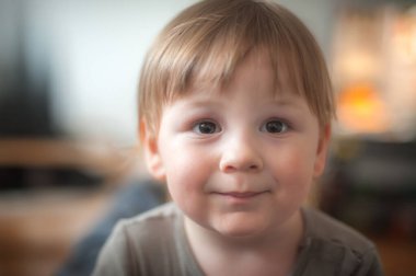 Neşeli, genç bir çocuk. Kapalı bir yerde rahatça otururken mutlu gözlerle ışıldıyor. Ortam sıcak ve davetkar bir atmosfer yayıyor, oyun zamanı için mükemmel..