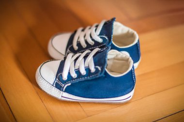 Bir çift şirin mavi bebek ayakkabısı parlak ahşap bir zeminde dinleniyor. Ayakkabılar beyaz bağcıklar ve genç kaşifler için ideal klasik detaylar içeriyor..