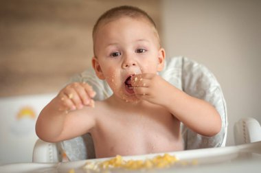 Yeni yürümeye başlayan bir çocuk ellerini kullanarak rahatça yemek yiyebilir. Etrafı rahat bir iç mekanla çevrili. Çocuk yemekle oynuyor, neşe ve merakla oynuyor..