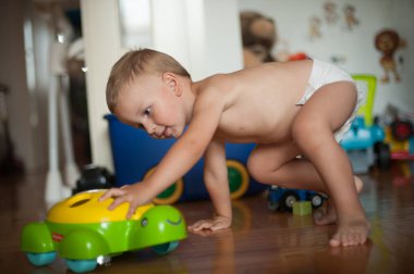Genç bir çocuk, parlak bir oyuncak arabayla etkileşime girerken neşeyle emekler. Bölge çeşitli oyuncaklar ve canlı dekorlarla dolu, canlı bir atmosfer yaratıyor..