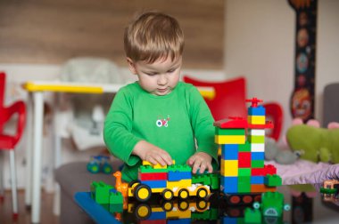 Genç bir çocuk, oyuncaklarla dolu sıcak, davetkar bir odada oynarken yaratıcılık ve odaklanma sergileyen canlı bloklarla dolu bir yapıyla meşgul olur..