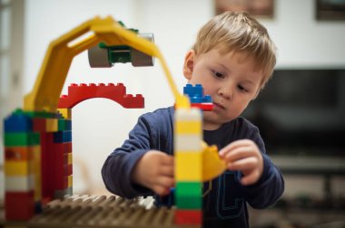 Genç bir çocuk, eşsiz bir yapı inşa ederken konsantrasyonunu ve yaratıcılığını sergileyerek, evindeki parlak ve renkli bloklarla meşgul olur..