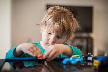 Genç bir çocuk, renkli oyuncak arabaları dikkatlice manipüle ederek oyun zamanı ile meşgul bir masada oturuyor. Parlak, neşeli atmosfer oturma odasında neşeli bir deneyim yaratıyor..