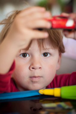 Bir çocuk, güneşli bir öğleden sonra, parlak bir mekanda renkli oyuncaklarla çevriliyken oyuncak arabalarla eğlenir, konsantrasyon ve merakını gösterir..