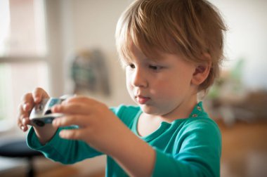 Küçük bir çocuk, odaklanmış ve meraklı, evde otururken oyuncak bir arabayı keşfediyor. Sıcak ışık odayı aydınlatıyor, neşeli bir atmosfer yaratıyor..