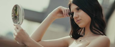 Genç bir kadın aynada kendine bakıyor. Sosyal medya içeriği için modern, kentsel bir ortamda poz veriyor. Modaya uygun ve modern görünüyor..