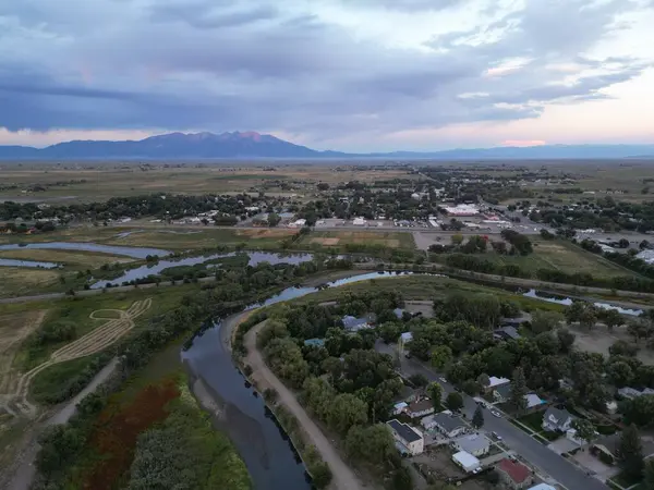 Nehir ve dağların dikey görüntüsü kırsal alanda parlak bir gökyüzünün altında yeşilliklerle çevrili.