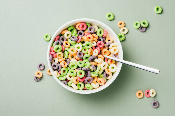 Colorful corn rings in bowl on green background. Ring-shaped sweet breakfast cereal with milk.