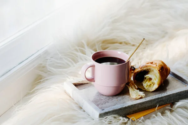 Cup of coffee with chocolate croissant on a tray, home cozy concept.