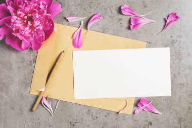 Davetiye ya da tebrik kartı maketi. Beton arka planda şakayık yaprakları olan bir zarf. Üst görünüm, alanı kopyala.