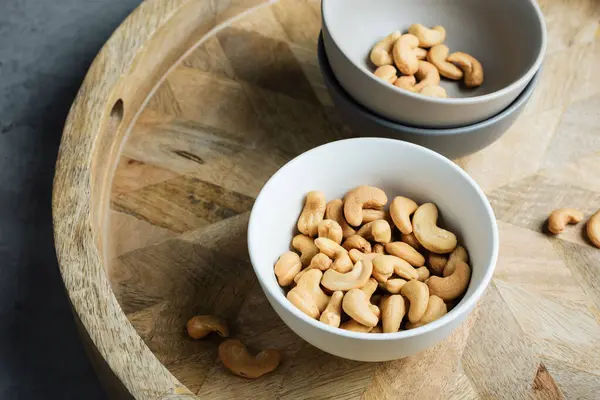 Roasted cashew nuts in a bowl on a wooden tray.