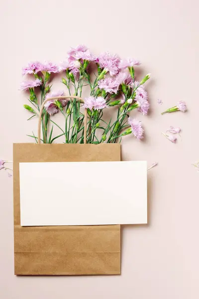 Pink carnation flowers in a paper bag, card mockup, copy space.
