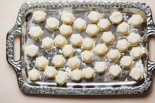 Raw homemade dumplings on a silver metal tray, top view.