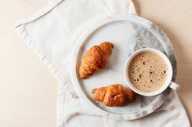 Cup of coffee with croissants on marble tray.