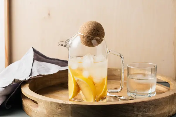 Water with lemon and ice on a wooden tray, refreshing drink.