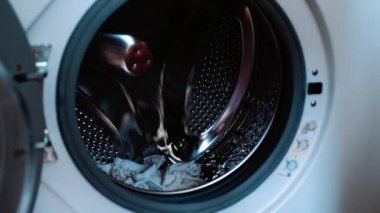 Çocuk kıyafetlerini yıkıyorum. Bir el çamaşır makinesinin variline çocuk kıyafetleri atıyor.