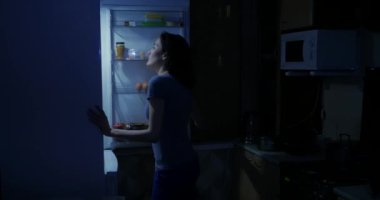 Bir kadın gece buzdolabını açar ve bir şişe su alır.