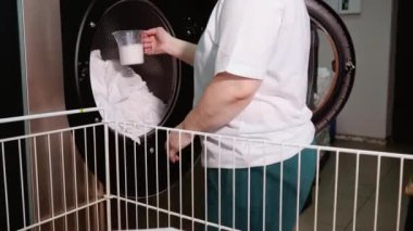 Çamaşır işçisi makineye çamaşır tozu döküyor.