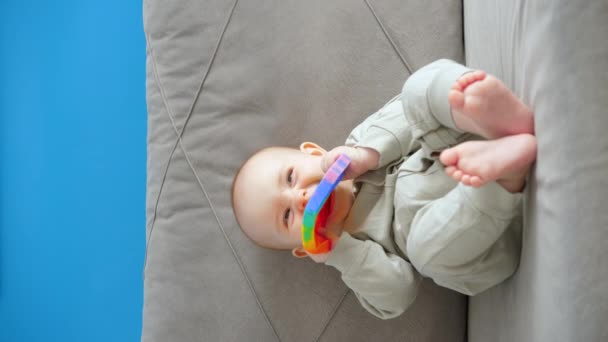 一个小孩坐在沙发上 手里拿着一个弹出的玩具 咬着它 垂直视频 — 图库视频影像