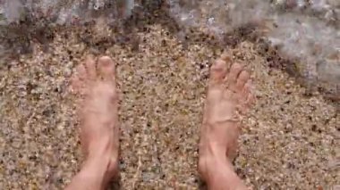 Köpüklü bir deniz dalgası bir adamın bacakları üzerinde yuvarlanıyor. Plaj tatili.