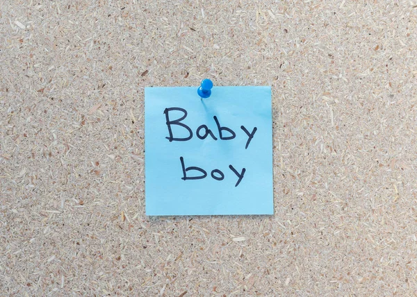 Surprise gender reveals hand written message on a a blue sticky note on a corkboard background with copy space