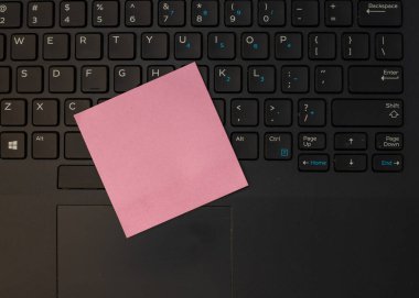 Siyah bir klavyede pembe, boş bir kağıt not.
